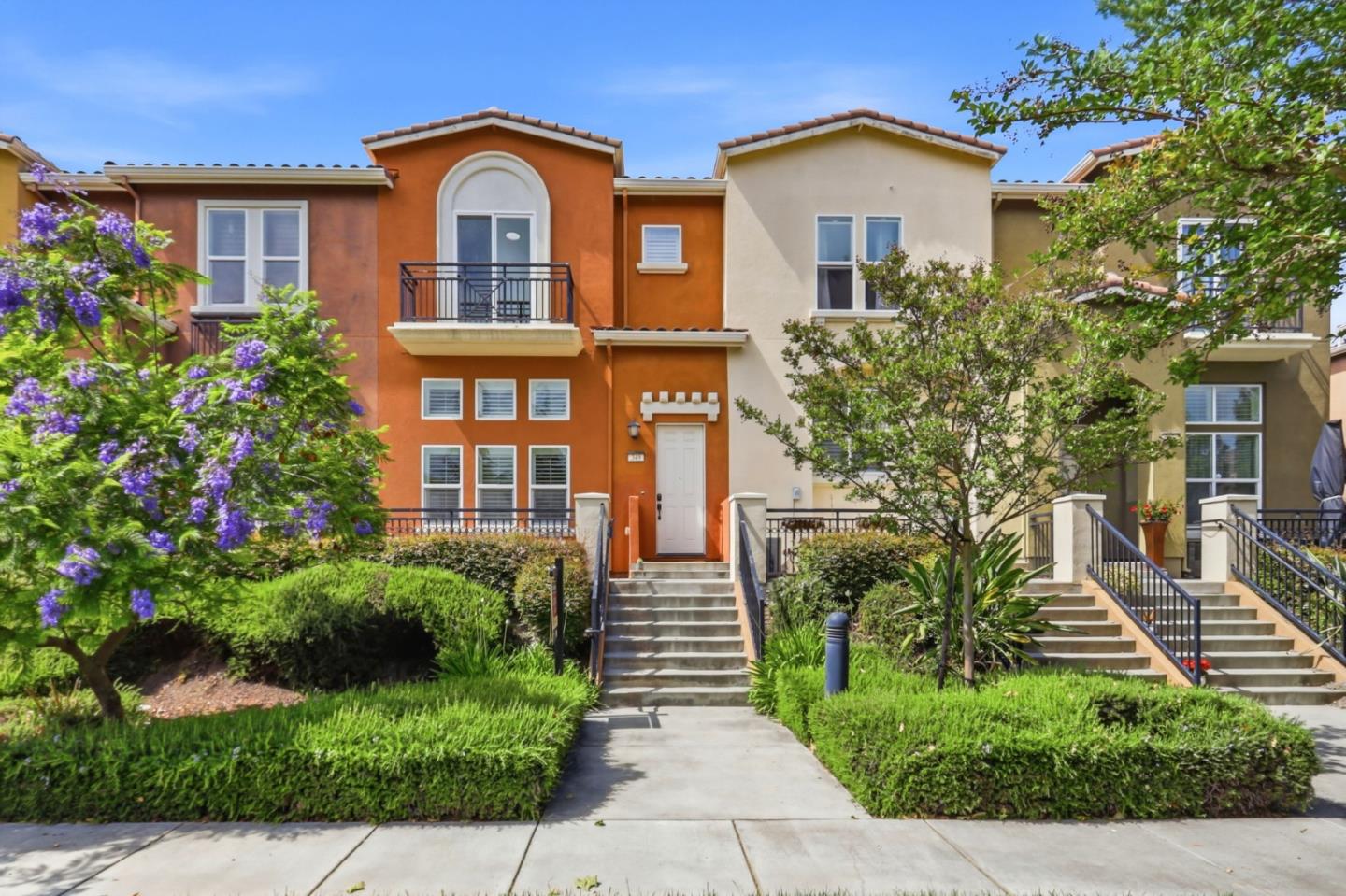 Terracotta-orange townhouse with an arched balcony window, front steps, and landscaped entry.
