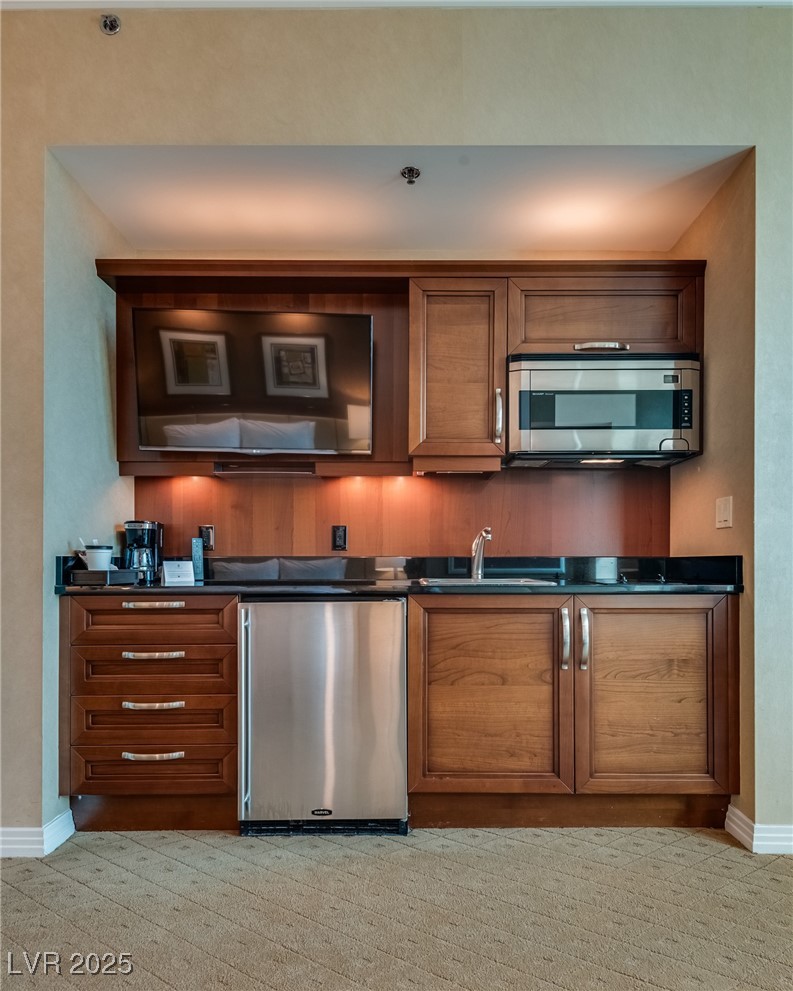 Compact kitchenette with warm wood cabinets, stainless-steel mini fridge, and a television built into the cabinetry.