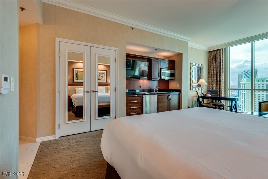 Furnished studio bedroom with a kitchenette and floor-to-ceiling windows overlooking nearby buildings.