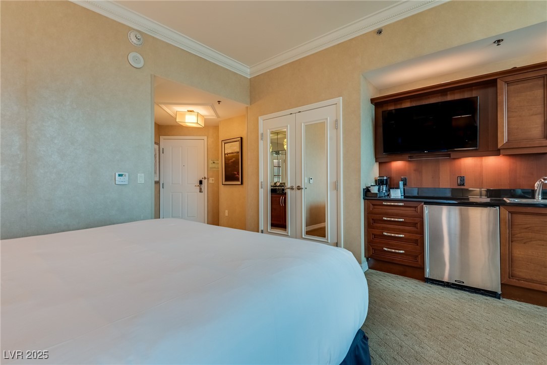 Bedroom with a large bed, mirrored doors, and a built-in kitchenette with television.