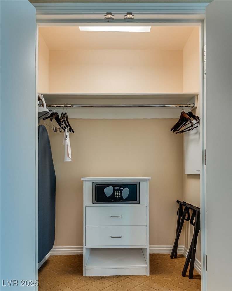 Walk-in closet with a safe-topped drawer unit, hanging rails, and folding luggage racks.