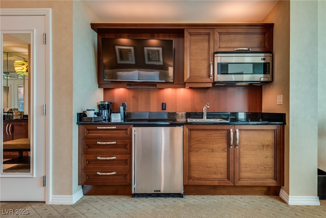 Compact kitchen with warm wood cabinets, black countertops, stainless-steel appliances, and a built-in television.
