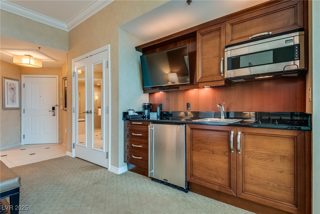 Kitchen with warm wood cabinets, black countertops, stainless-steel appliances, and a television above the counter.