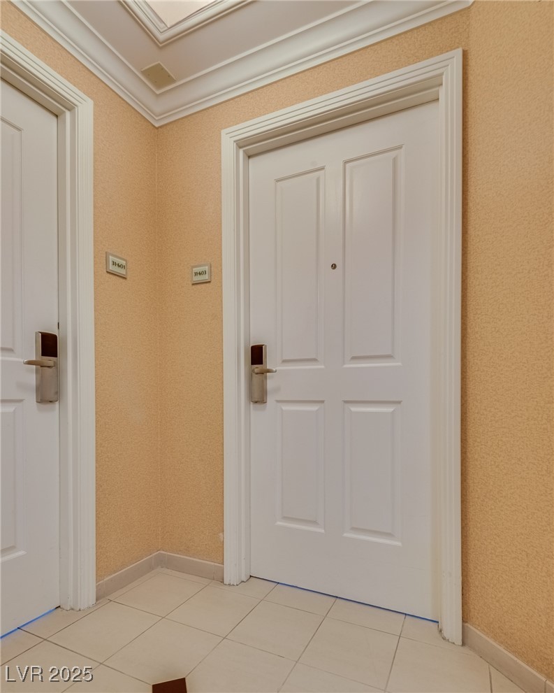 Unit entry with a white paneled door, beige textured walls, and tiled flooring.