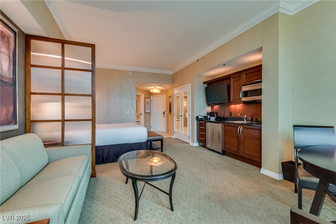 Furnished studio suite with a bed, pale sofa, and compact wood-cabinet kitchenette.