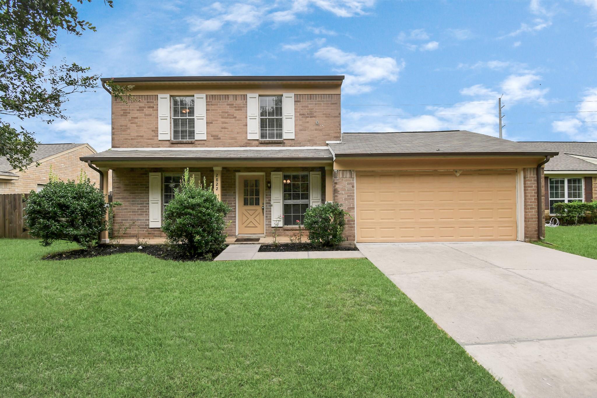Two-story brick house with white shutters, a tan door, and a wide garage.