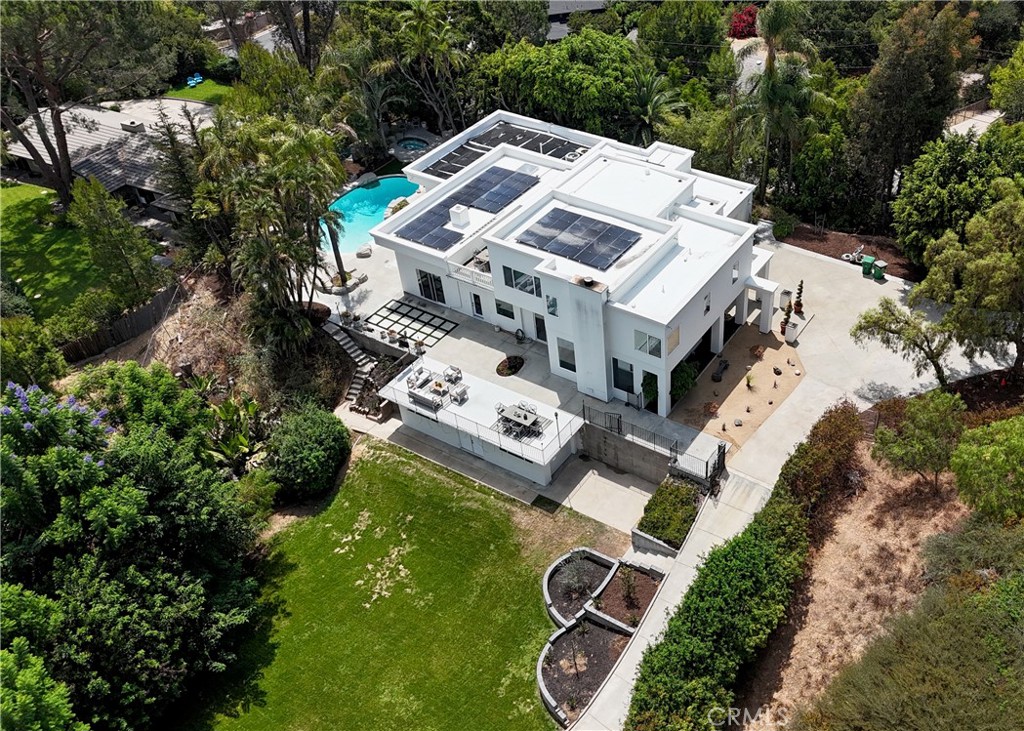 Modern white home with rooftop solar panels, a swimming pool, and a landscaped yard.