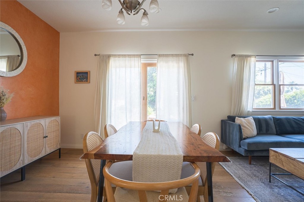 Dining area with a long wooden table and woven chairs beside a blue sofa and orange accent wall.