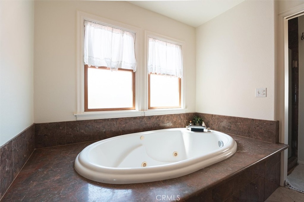 Bathroom with a white oval soaking tub beneath two lace-curtained windows.