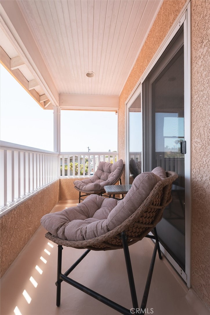 Covered balcony with cushioned wicker chairs, a small table, white railing, and sliding glass door.