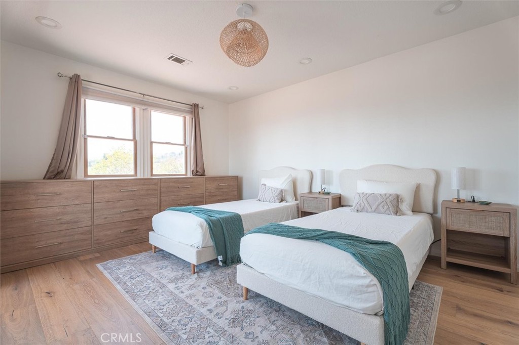 Staged bedroom with two beds, teal throws, and a long wood dresser beneath the windows.
