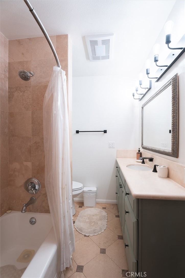 Bathroom with tan tile, a curtained bathtub, and a long vanity beneath an ornate mirror.