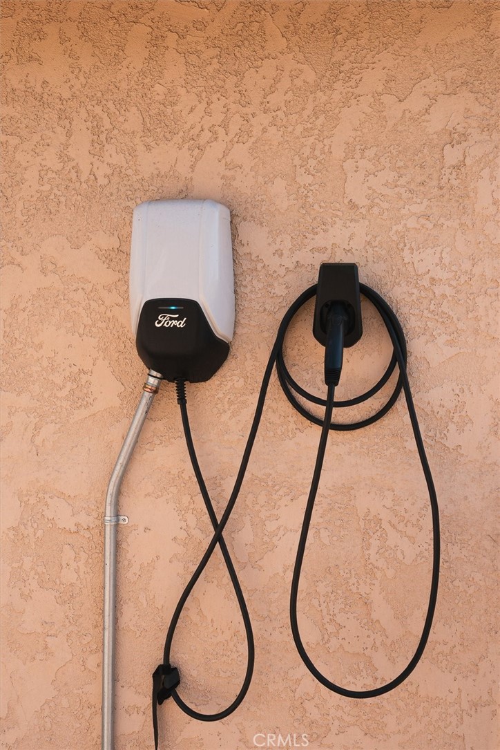 Ford electric vehicle charger mounted on a textured stucco wall, with its cable hanging beside it.