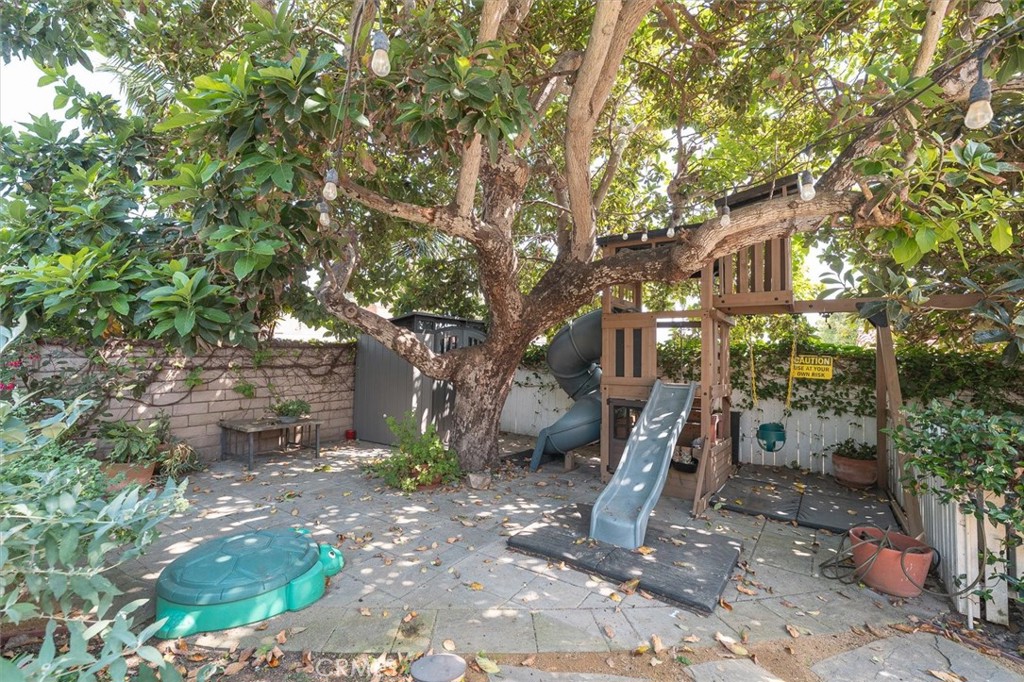 Shaded backyard with a large tree and wooden play structure with slide and swings.