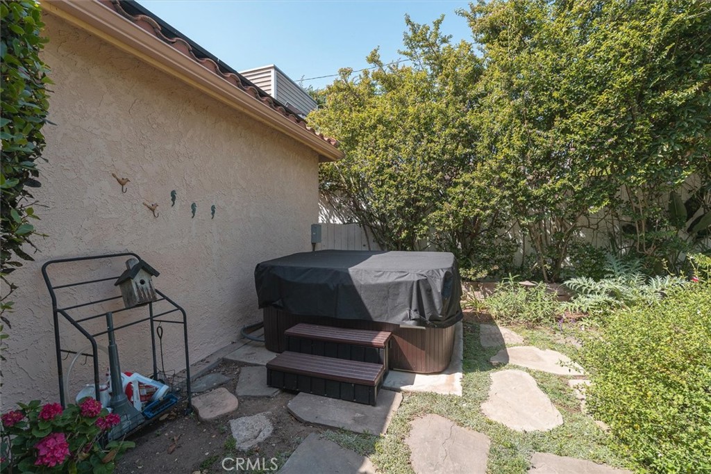 Backyard patio with a covered hot tub, stepping stones, and leafy garden plants.