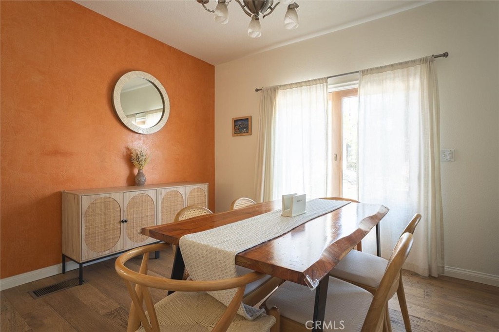 Dining room with a long wooden table, orange accent wall, and woven-front sideboard.