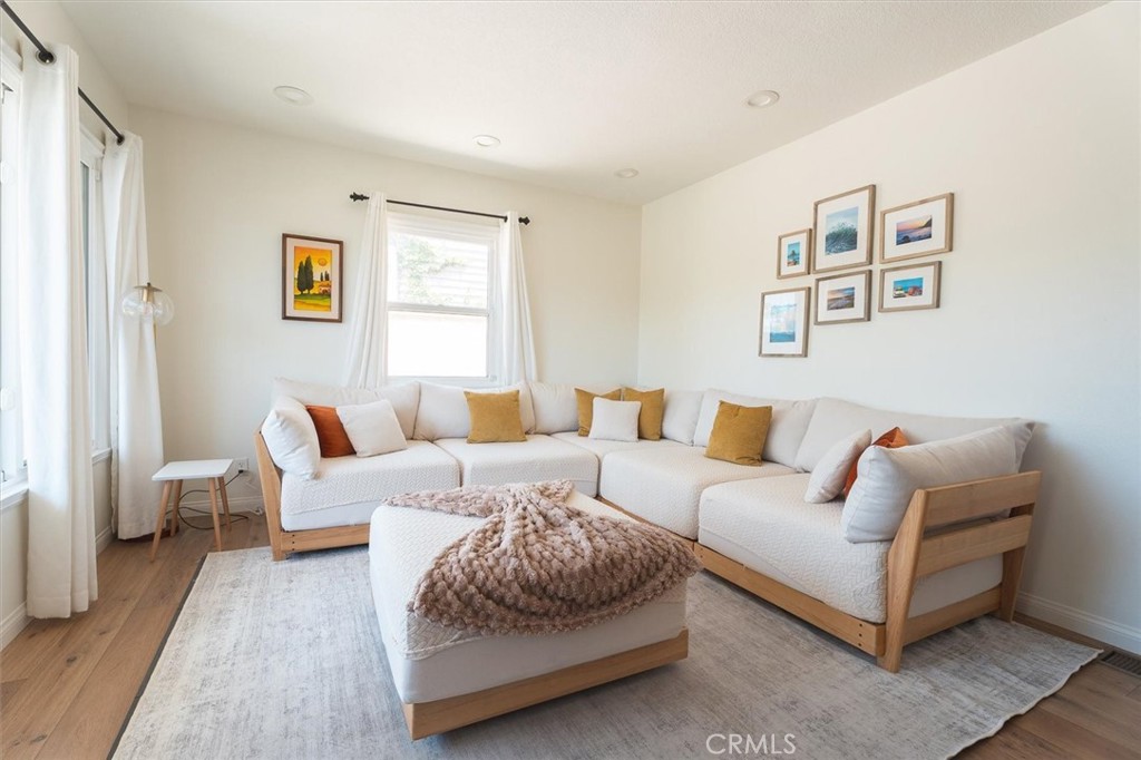 Staged living room with a white sectional, mustard accent pillows, and large curtained windows.