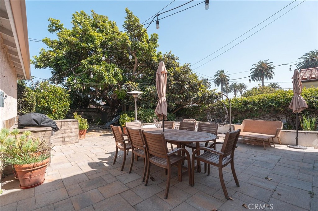 Backyard patio with a wooden dining set, closed umbrellas, and mature trees.