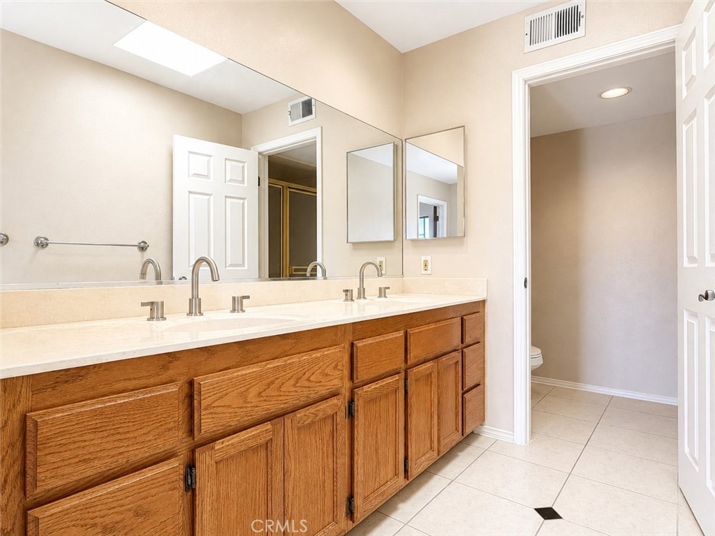 Bathroom with a double-sink vanity, oak cabinets, large mirrors, and tiled flooring.
