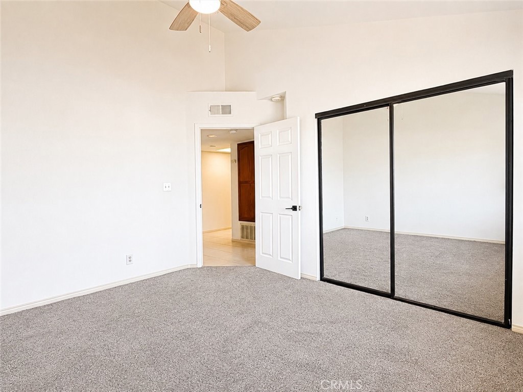 Empty bedroom with gray carpet, a ceiling fan, and mirrored sliding closet doors.