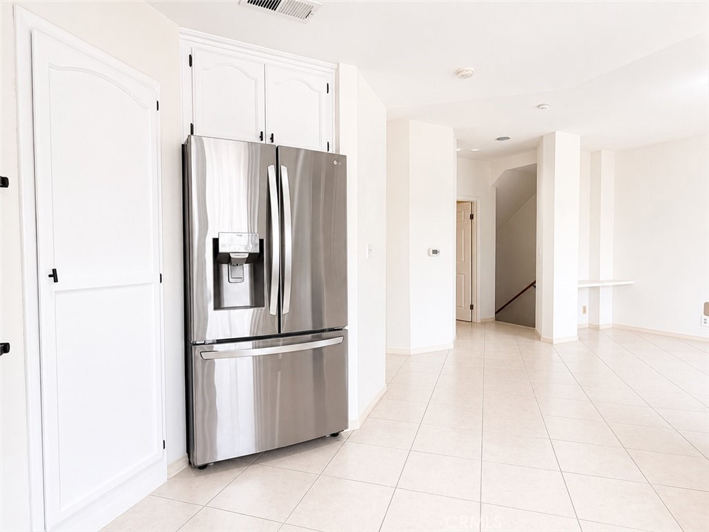 Kitchen with white cabinets, stainless steel refrigerator, and tiled floor opening toward a staircase.