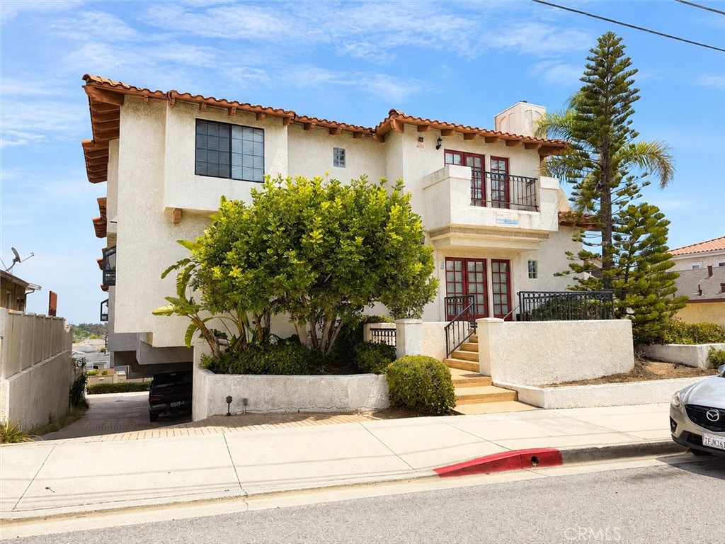 Stucco residence with terracotta roof, balconies, red-framed doors, and landscaped frontage.