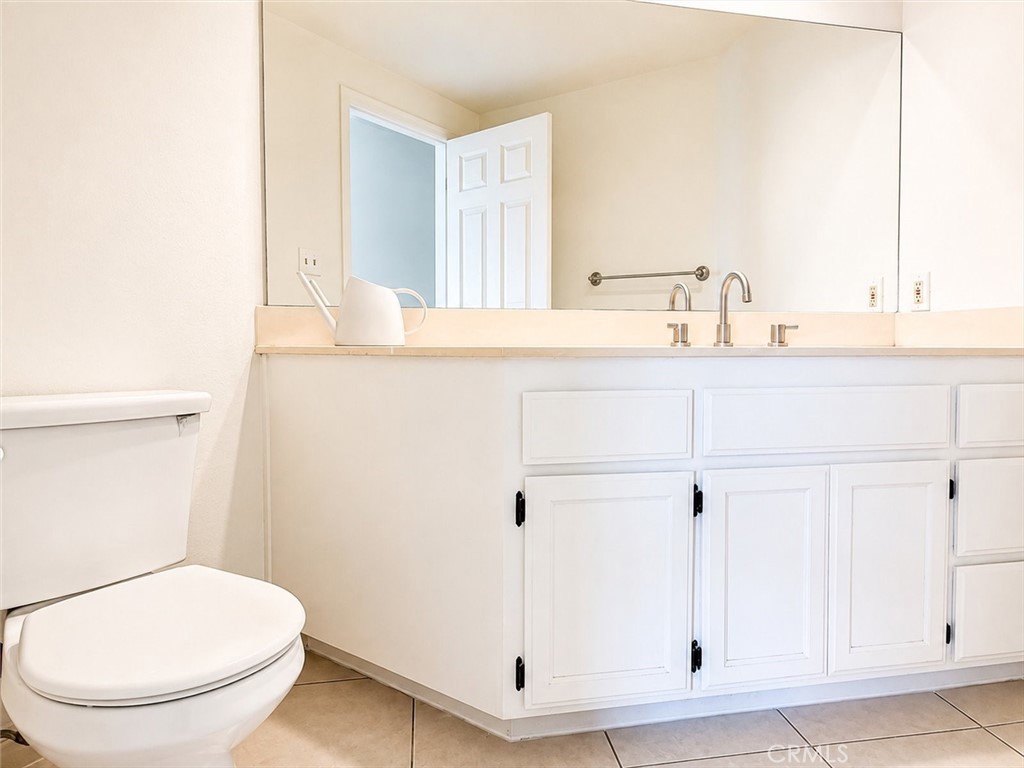 Bathroom with a white toilet and long paneled vanity beneath a large mirror.
