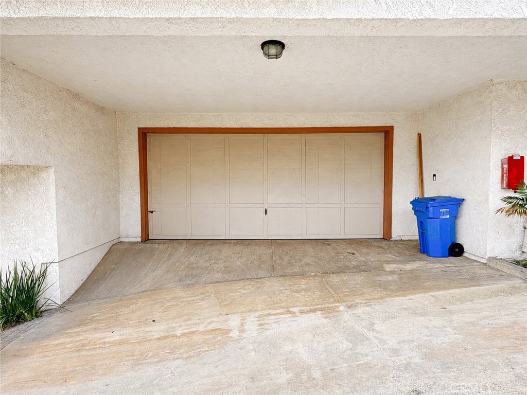 Covered driveway and closed garage with a blue recycling bin beside the door.