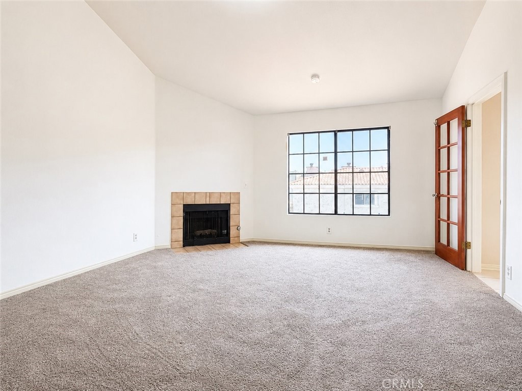 Empty living room with a tiled fireplace, carpeted floor, and large grid window.