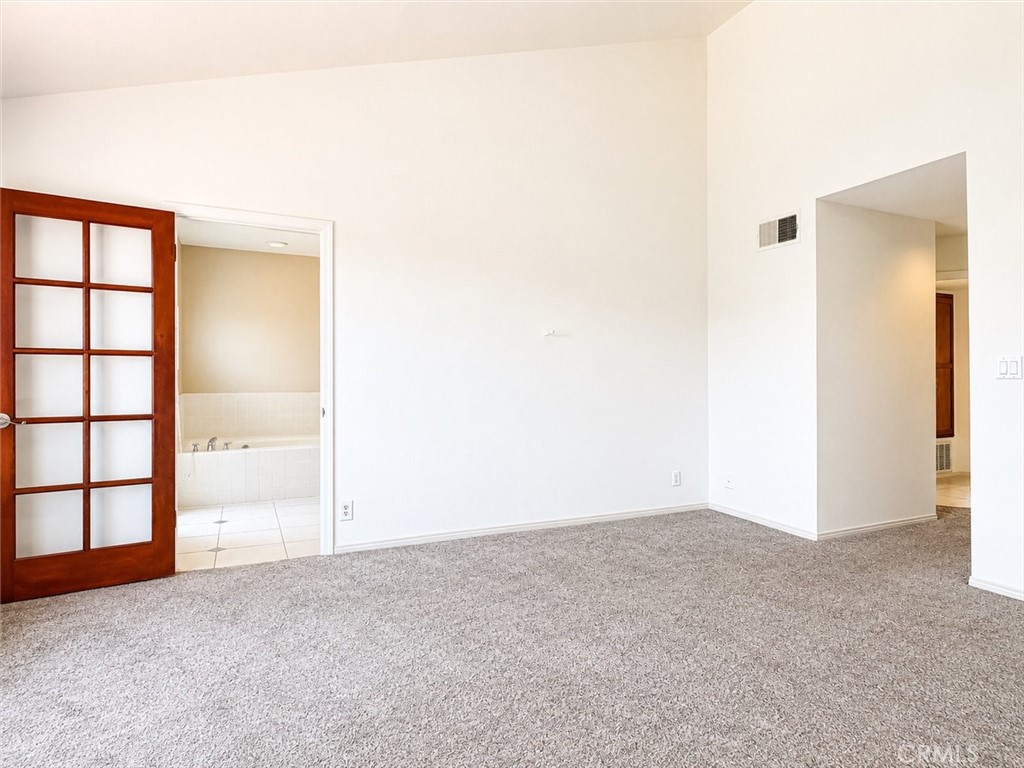 Empty carpeted room with a wood-framed glass-panel door opening to a tiled bathroom.