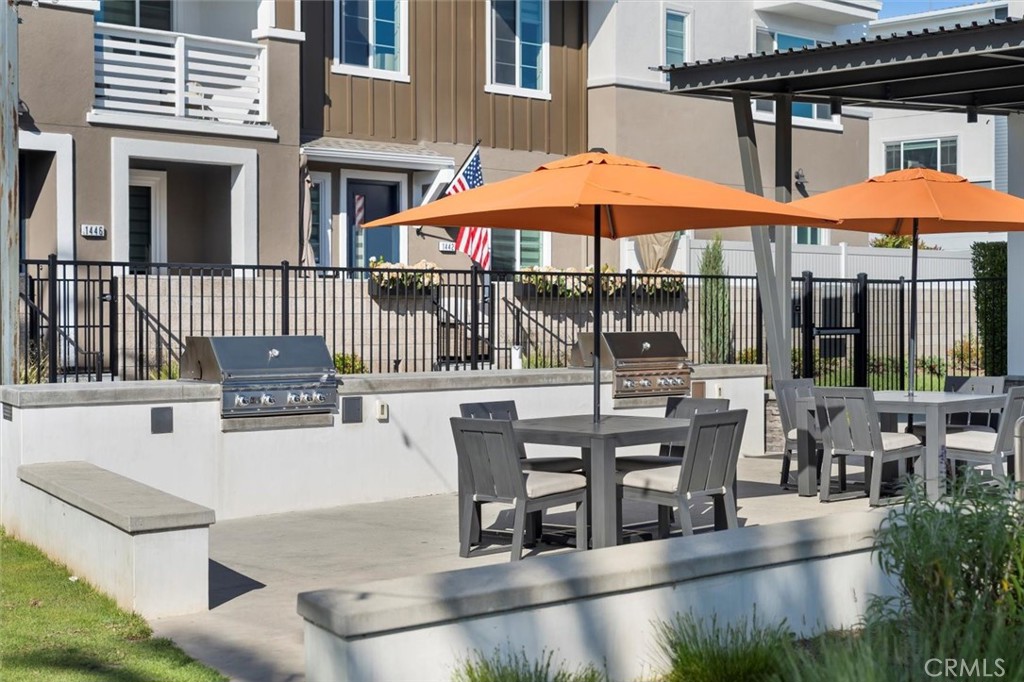 Shared residential patio with orange umbrellas, dining tables, and built-in gas grills.