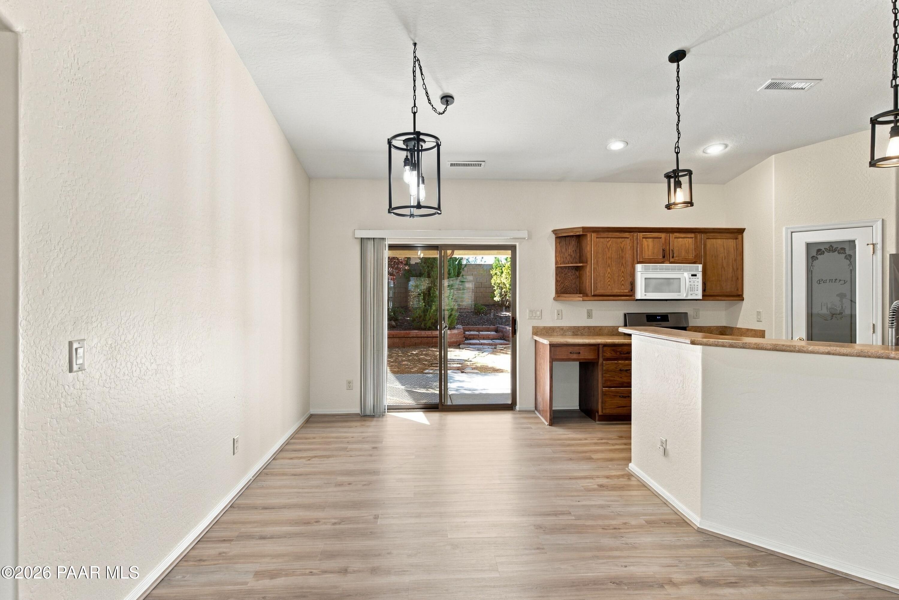 Vacant kitchen and dining area with wood cabinets, breakfast bar, and sliding glass door to the patio.