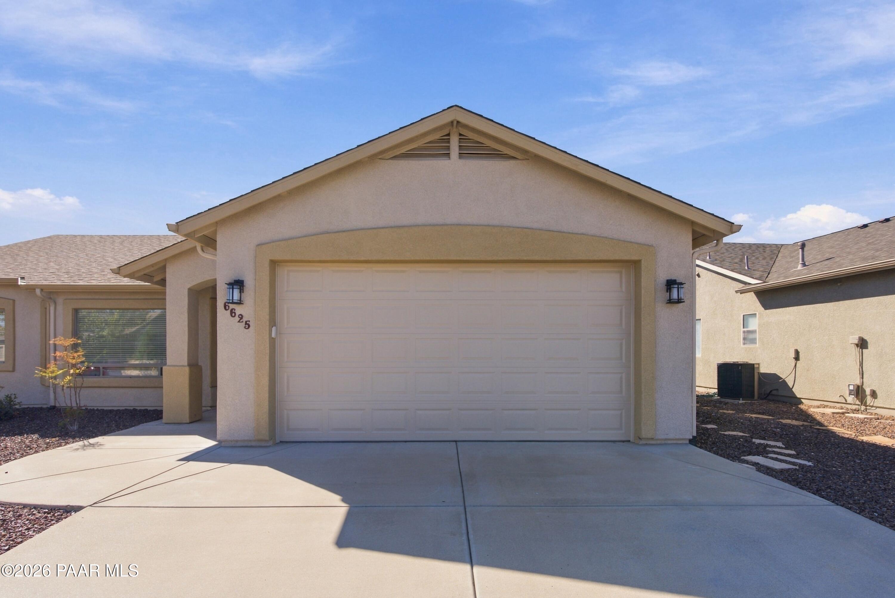 Stucco home with a gabled roof, two-car garage, and wide concrete driveway.