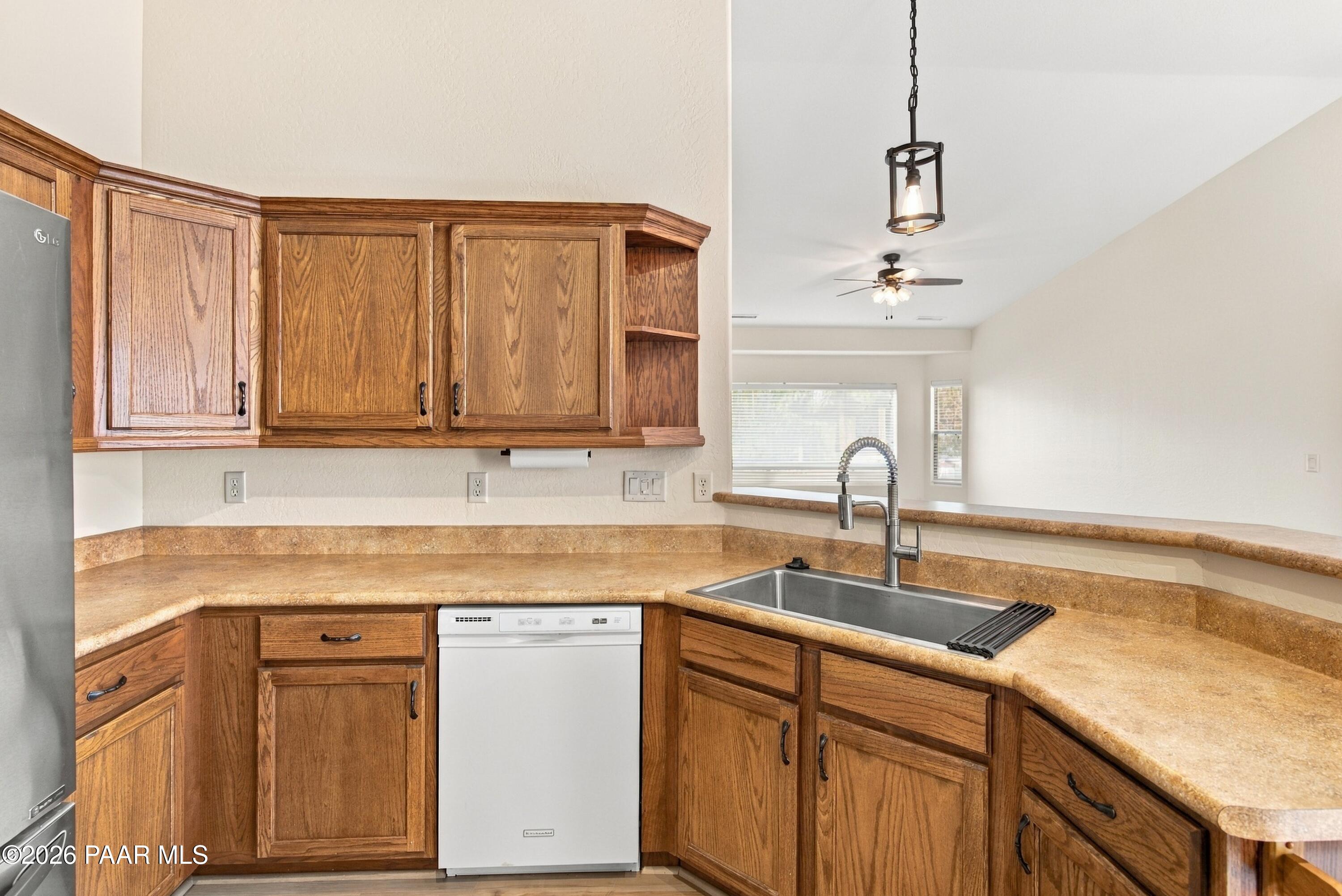 Kitchen with warm wood cabinets, tan counters, and a stainless steel sink beneath a spring faucet.