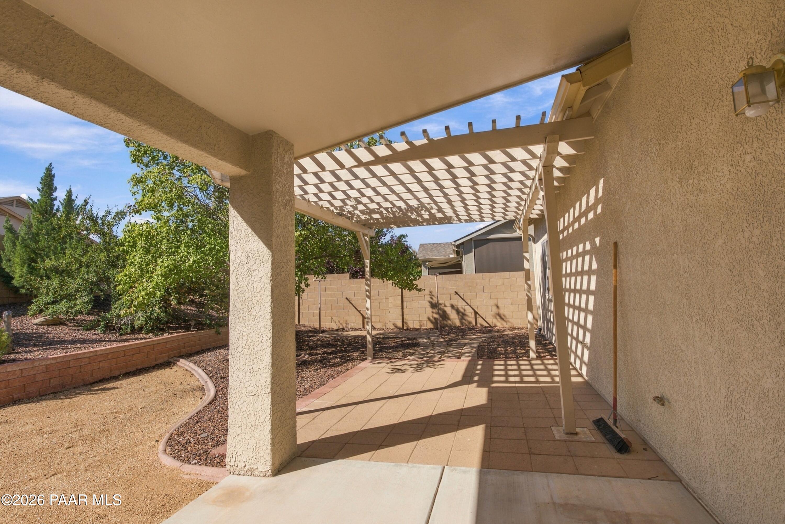 Covered backyard patio with a tiled floor, pergola, and gravel landscaping.