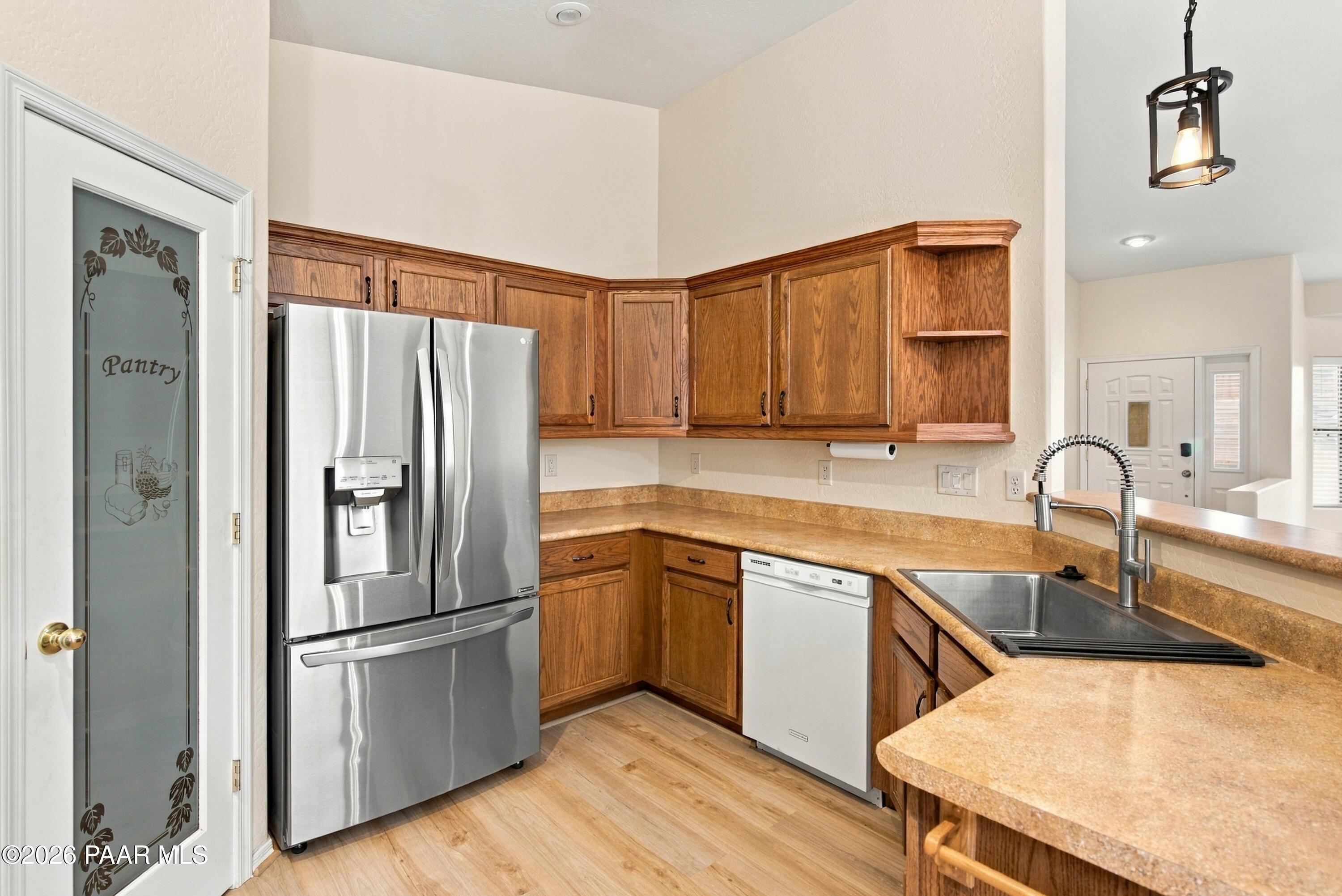 Kitchen with wood cabinets, tan countertops, stainless steel appliances, and a frosted-glass pantry door.