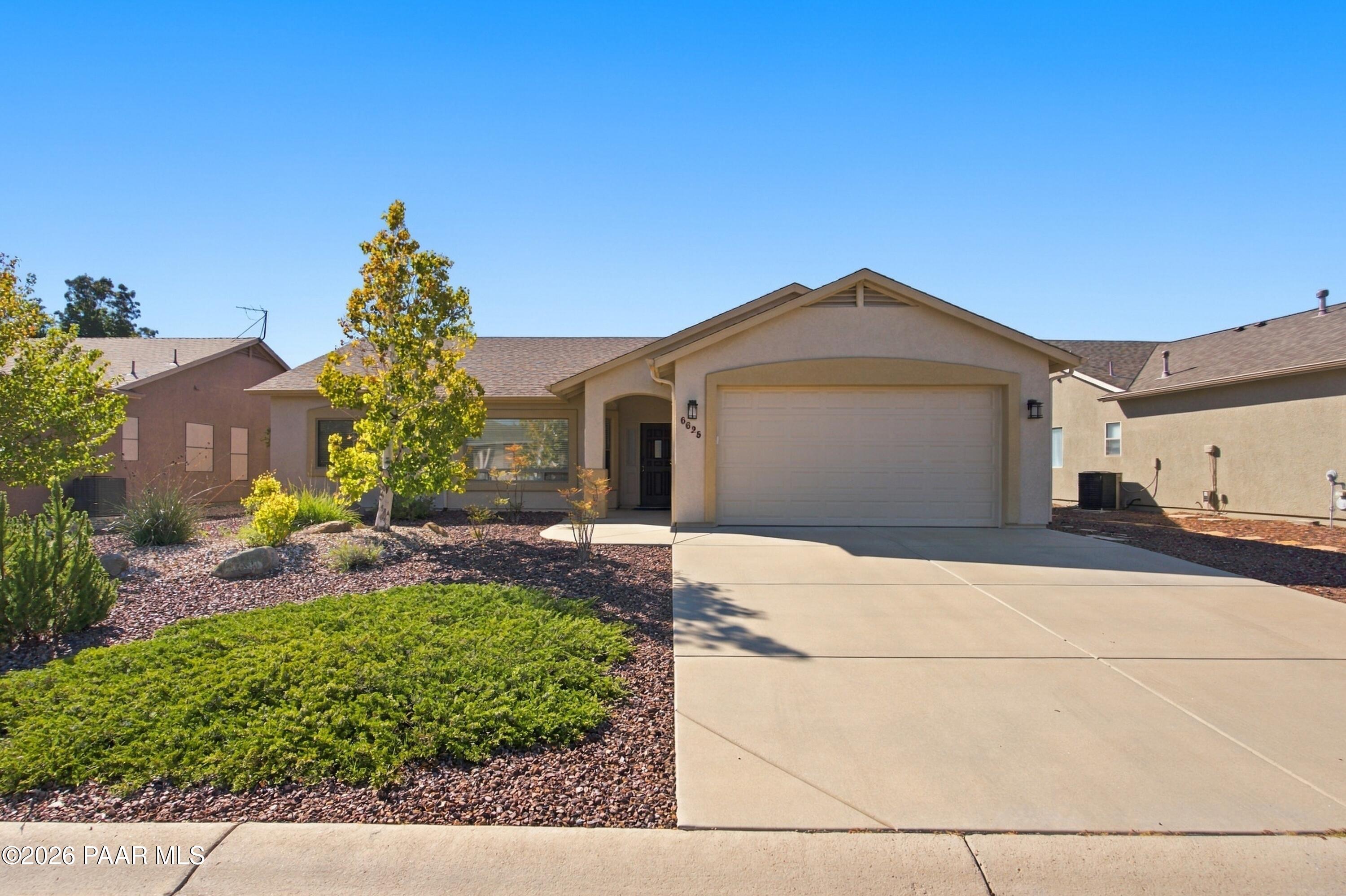 Single-story home with a two-car garage, broad driveway, and landscaped rock yard.