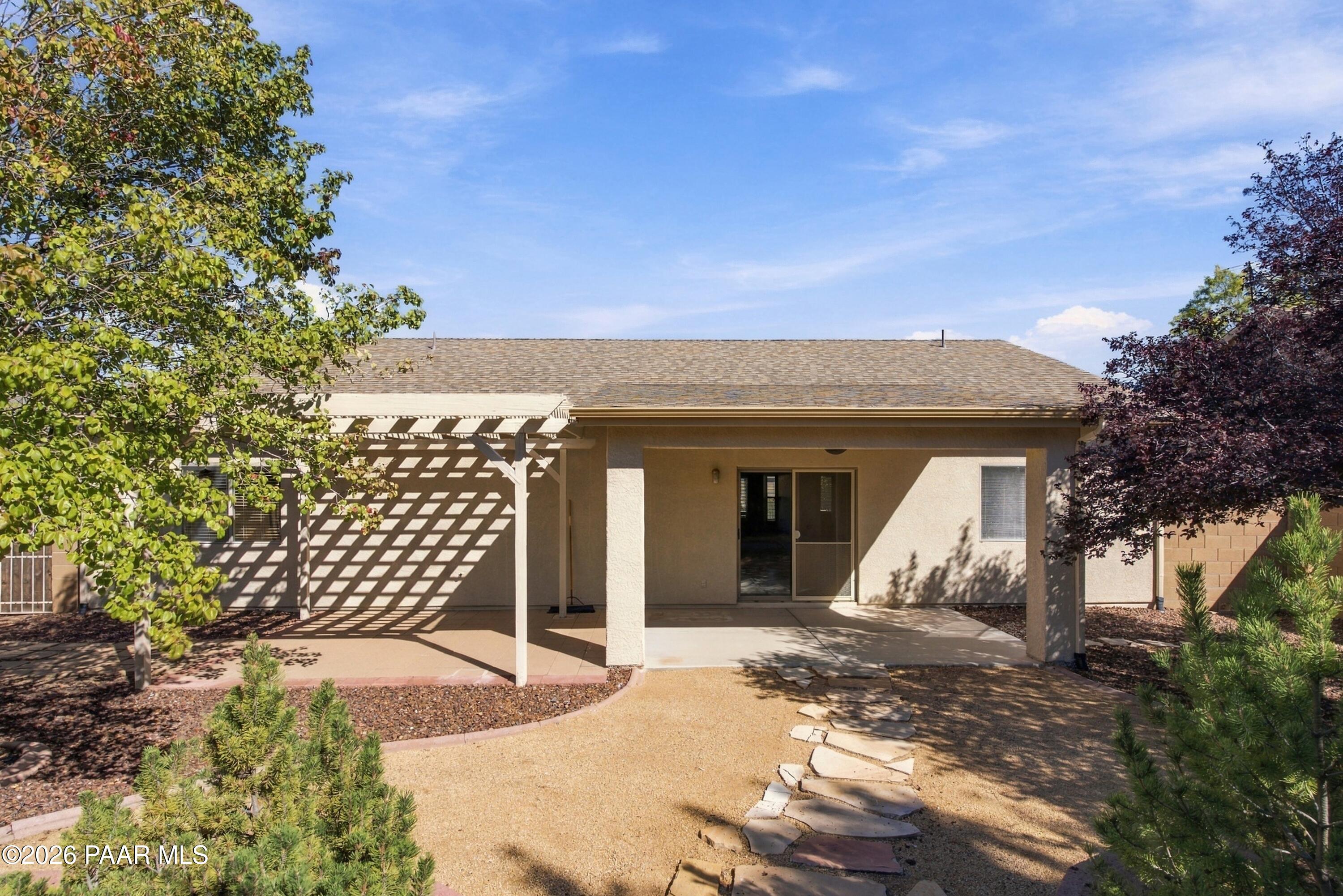 Single-story home’s rear patio with a lattice pergola, sliding glass door, and stepping-stone path.