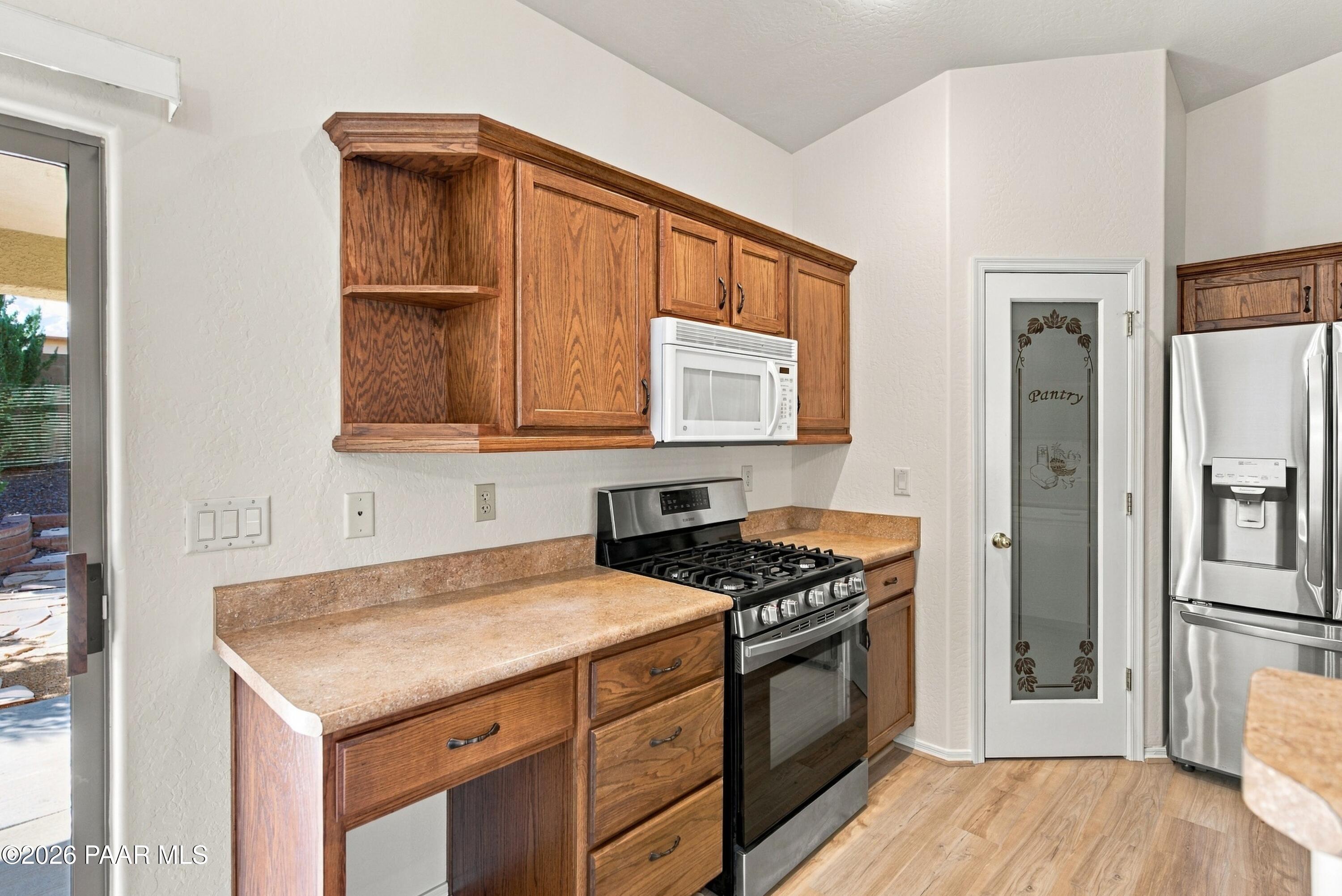 Kitchen with warm wood cabinets, tan countertops, stainless steel appliances, and a glass-paneled pantry door.