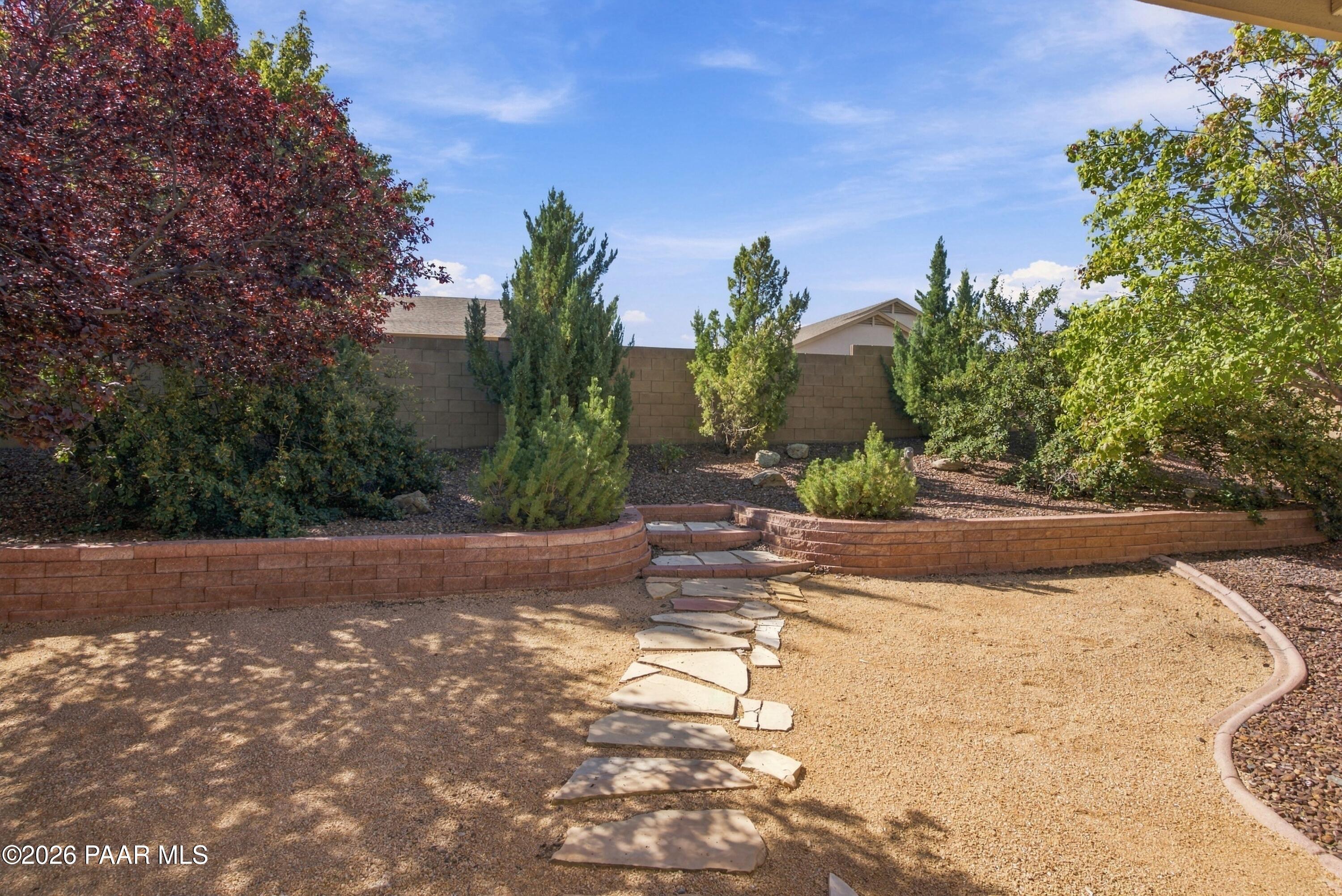 Backyard with a gravel courtyard, stepping-stone path, raised brick beds, and mature trees.