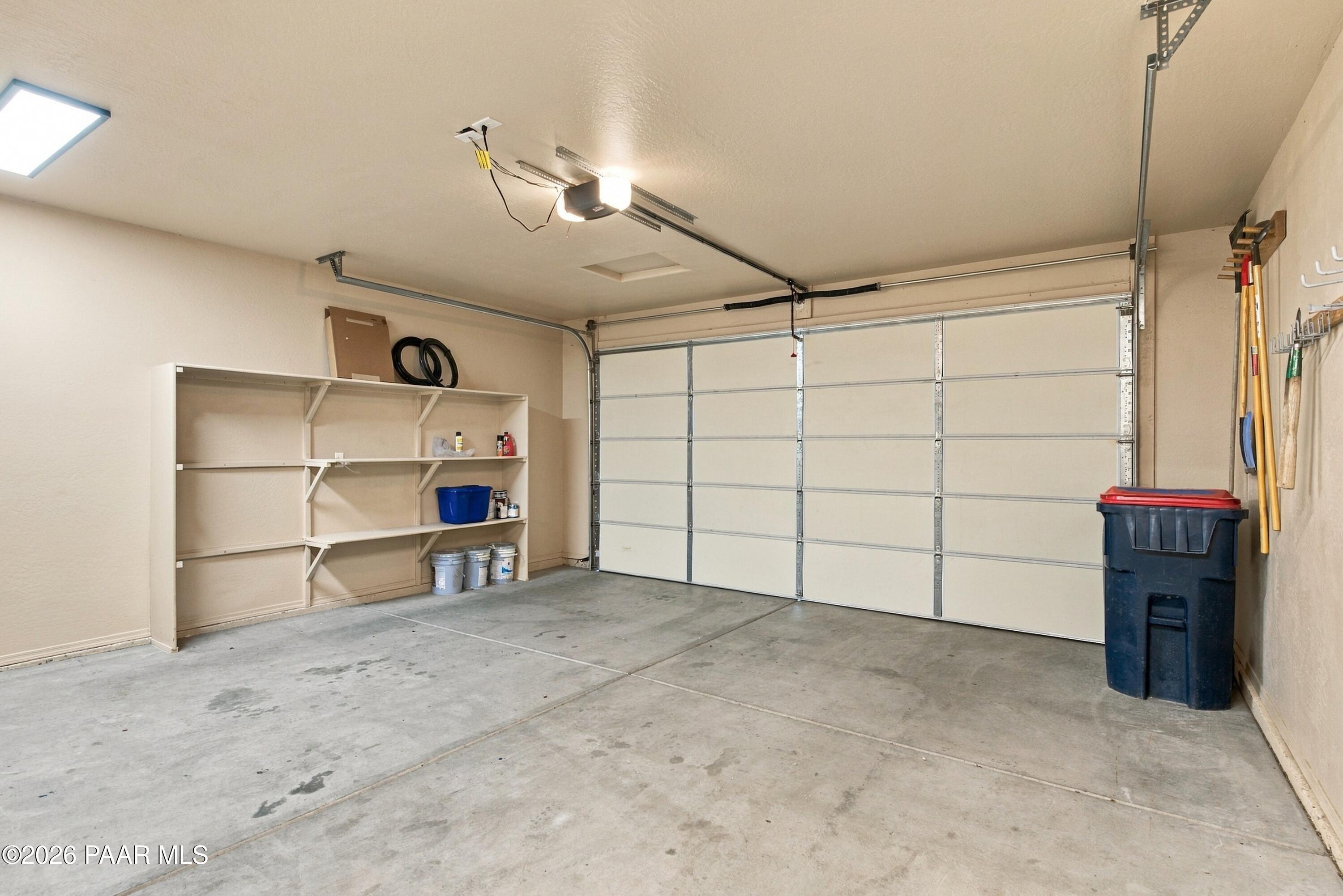 Garage with a closed sectional door, concrete floor, storage shelves, and tools hung on the wall.