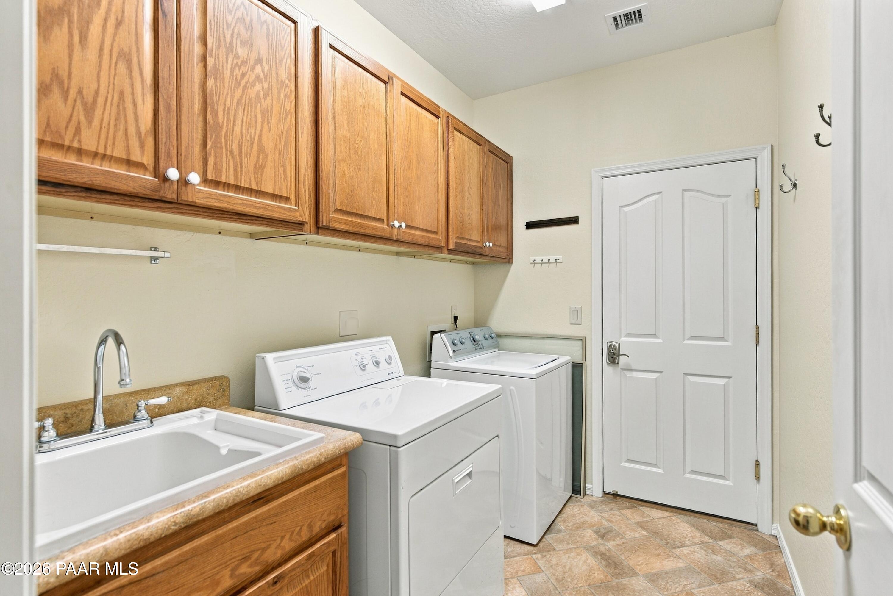 Laundry room with washer and dryer beneath wood cabinets, beside a utility sink.