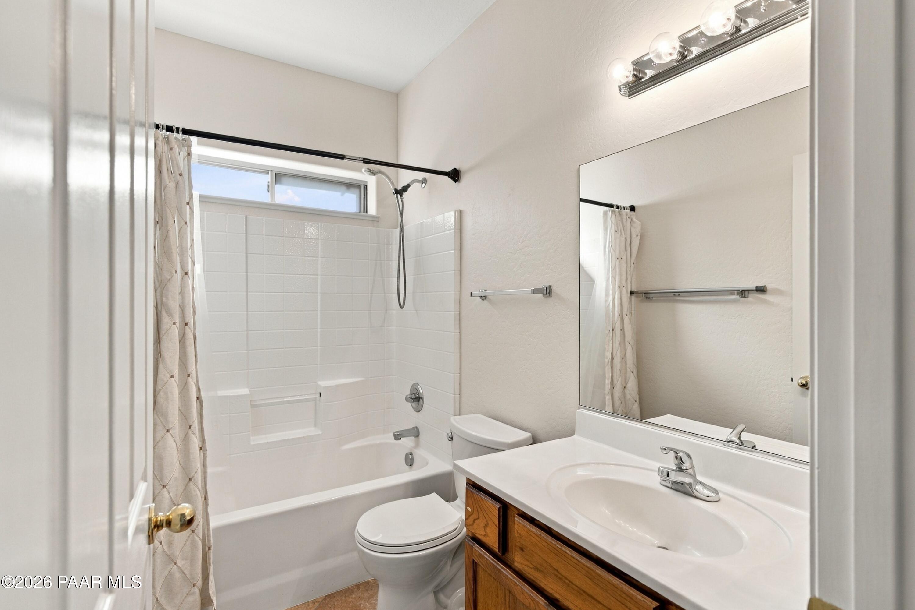 Bathroom with a white tub and tiled shower, toilet, and wood vanity beneath a large mirror.