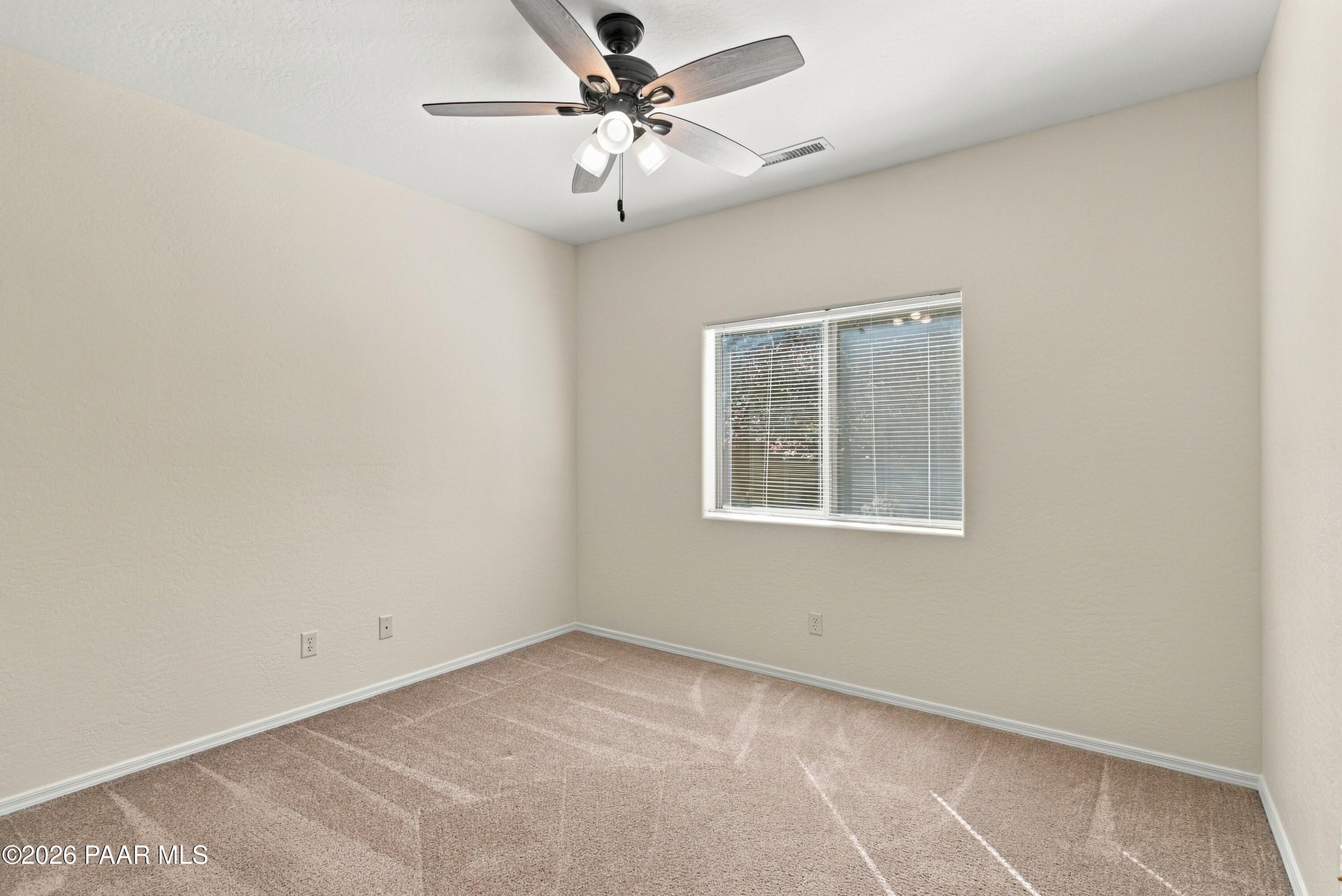 Empty bedroom with beige carpet, a window with blinds, and a ceiling fan.