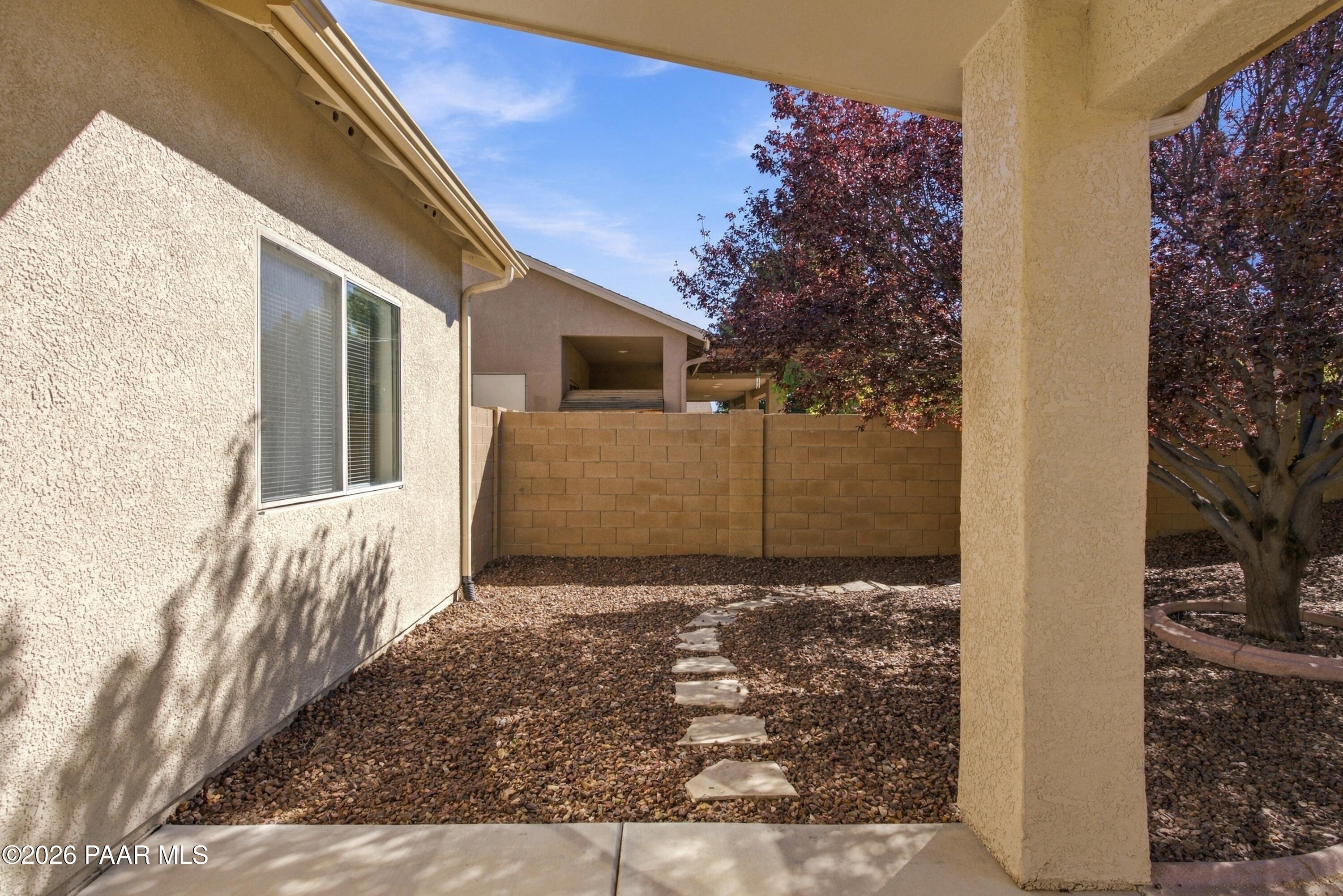 Covered rear patio and gravel yard with stepping stones and a mature tree.
