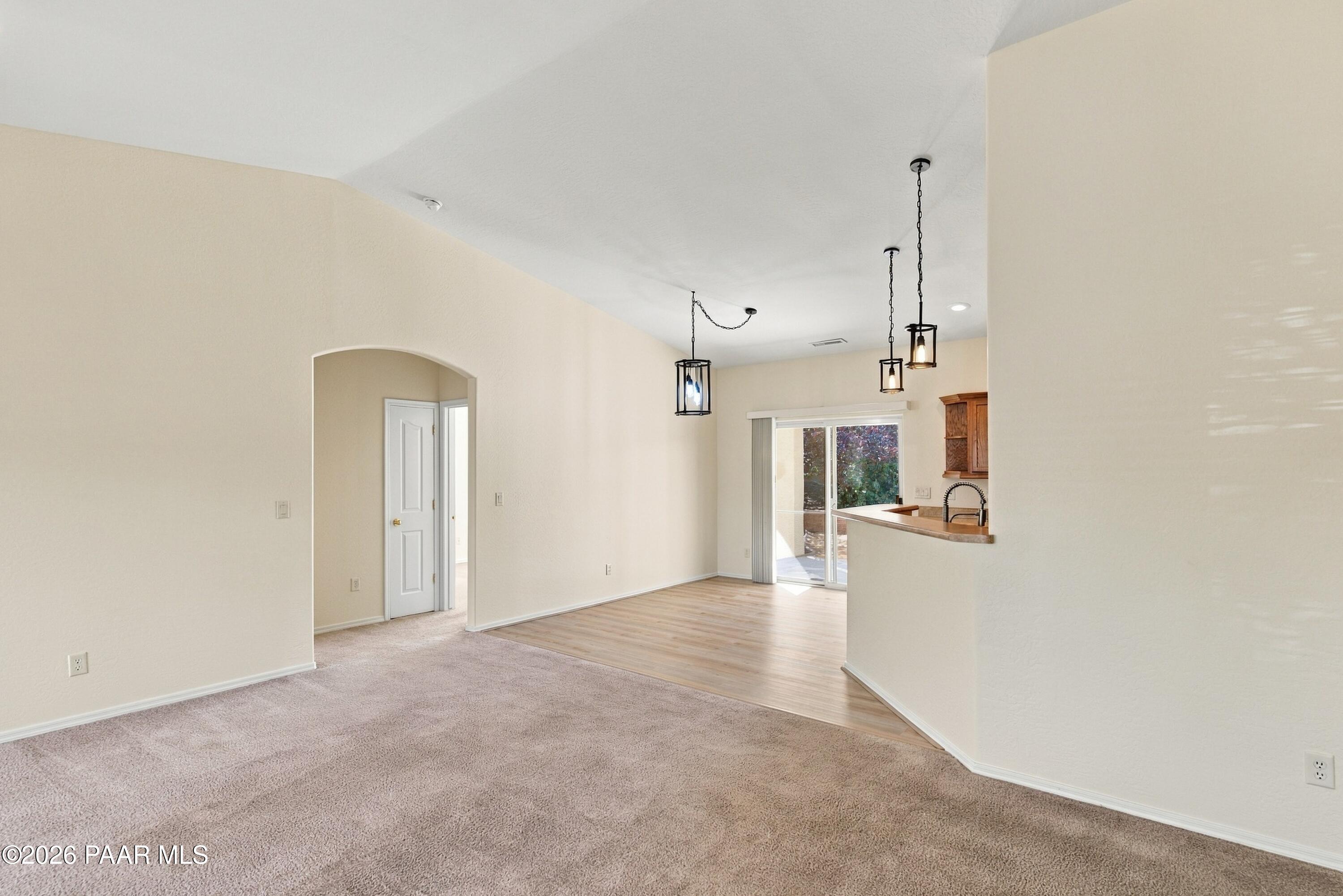 Empty living and dining area with carpet, wood flooring, pendant lights, and a kitchen breakfast bar.
