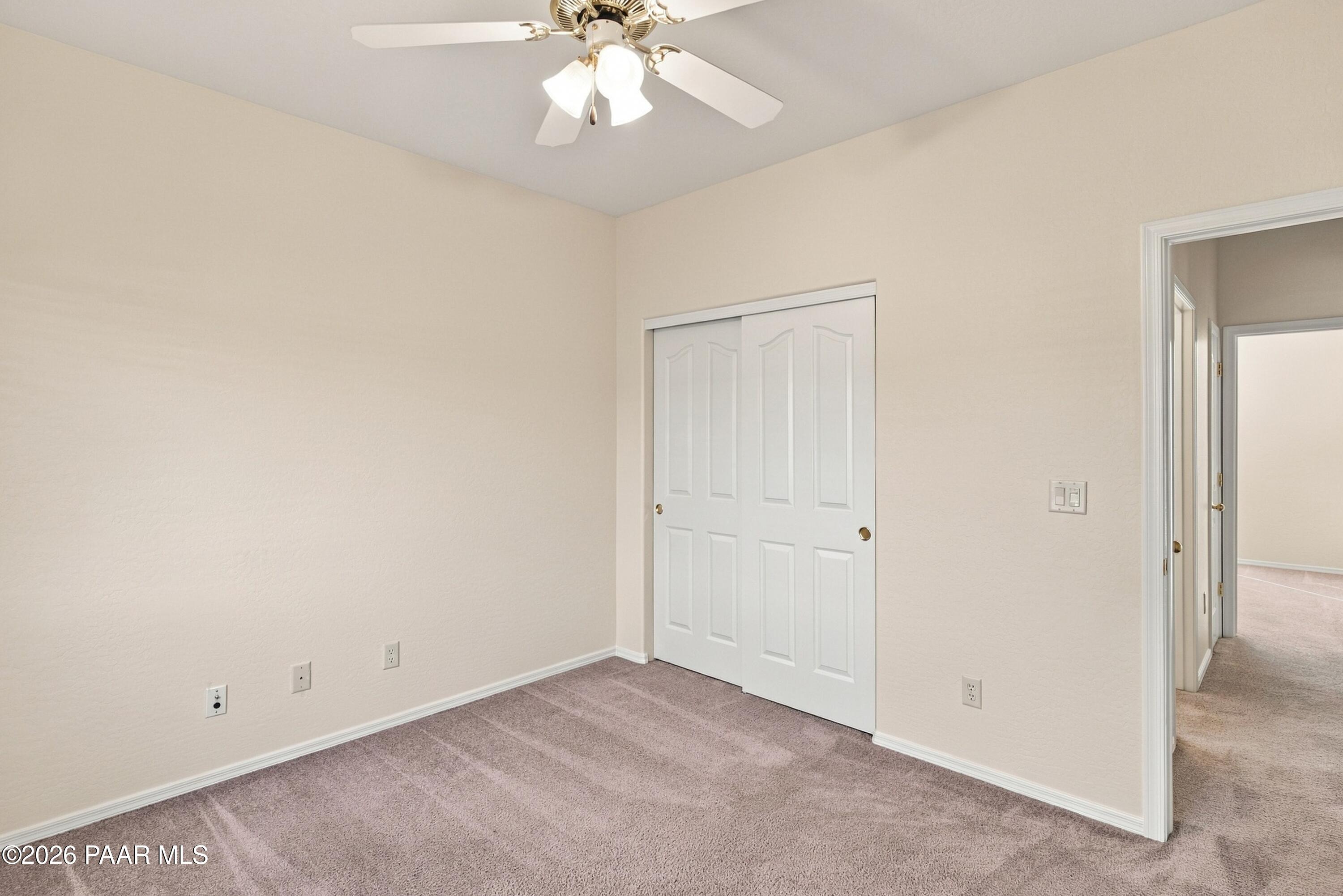 Empty bedroom with mauve carpet, a white double-door closet, and a ceiling fan with lights.