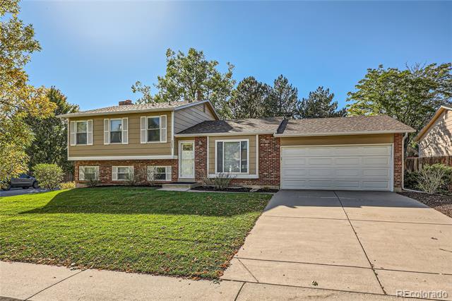 Split-level home with tan siding, brick accents, two-car garage, and wide driveway.