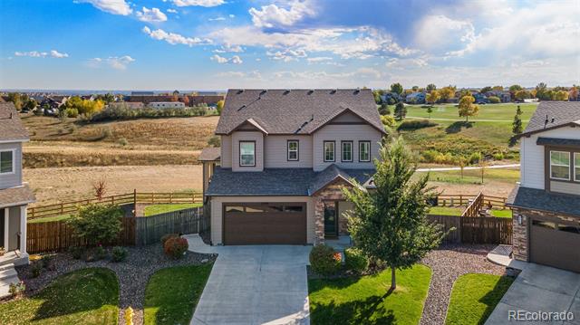 Two-story home with a two-car garage, fenced yard, and open fields behind it.