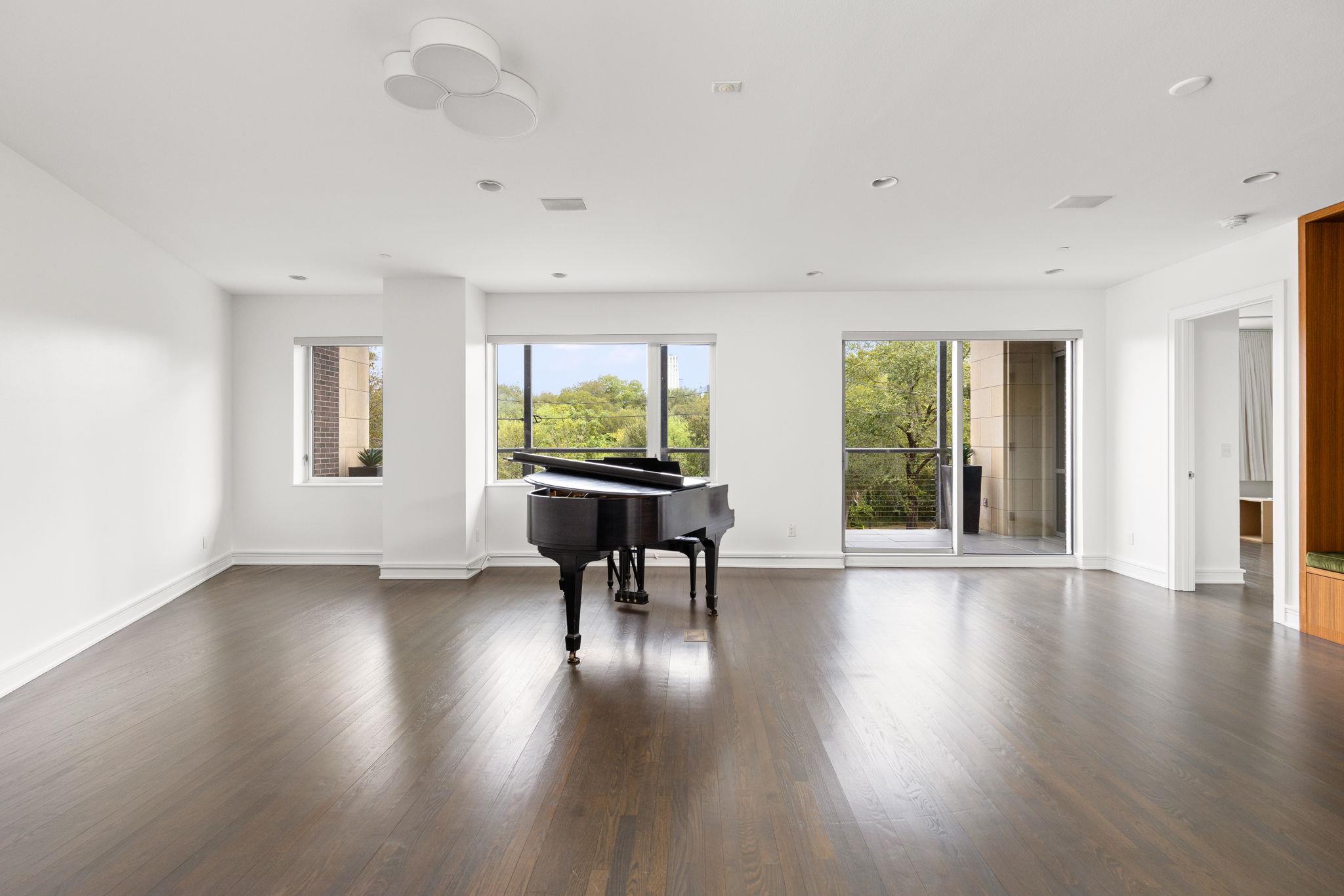 Bright condo living room with a black grand piano, dark wood floors, and windows overlooking trees.